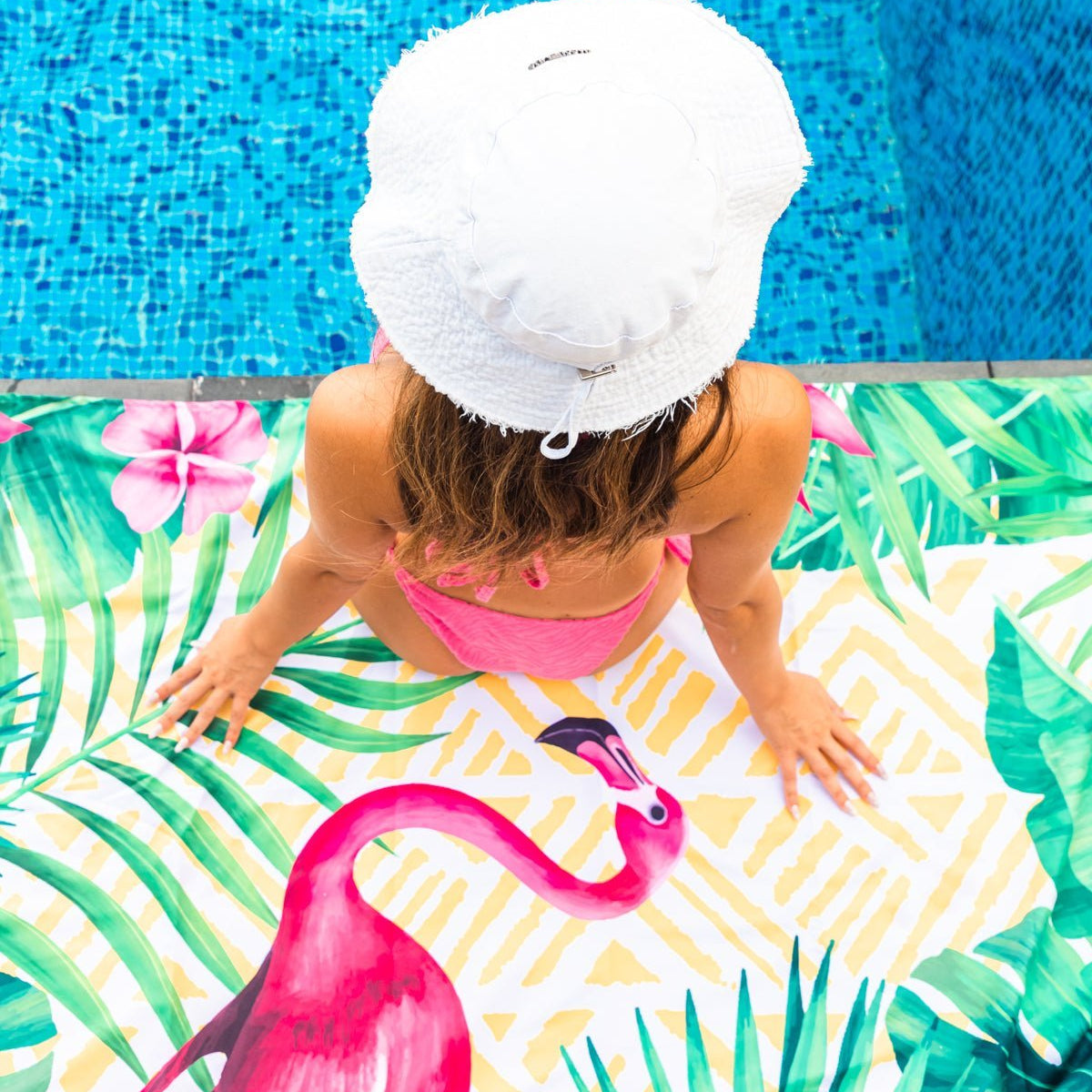 A girl sitting on the pool on a Quick Dry, Sand Free, Light Weight, Compact and Ecofriendly Microfiber Beach Towel from La Toalla