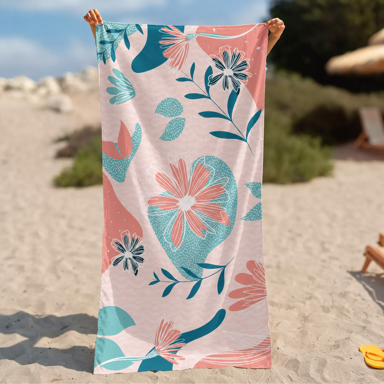 A beach towel from La Toalla with a pink, teal, and coral floral pattern is held up by a person&