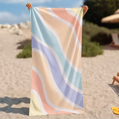 A rectangular beach towel with a pastel wavy stripe pattern in peach, light blue, lavender, and cream, held up by a person&