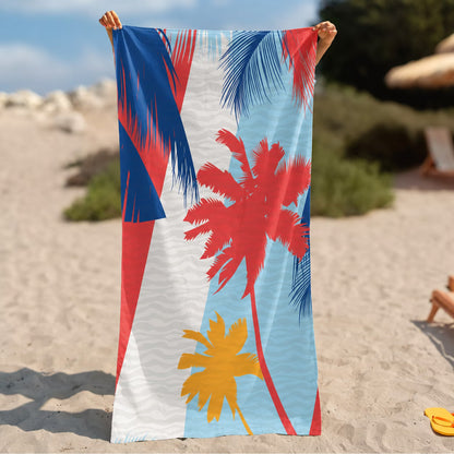 A beach towel with a tropical palm tree print in red, blue, yellow, and white, held up by a person on a sandy beach.